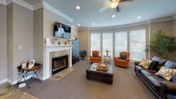 This single-floor space is thoughtfully designed to create a warm and professional atmosphere. The entry reception area features large-format stone tile flooring in earthy tones, recessed lighting, and crisp crown molding. A centrally positioned desk with seating for visitors establishes a welcoming focal point, while a mirrored accent wall adds depth and brightness to the space.

Transitioning into the main lounge area, the flooring shifts to plush carpet, enhancing the comfortable and relaxed ambiance. A standout white-mantled fireplace with a stone surround serves as the room's centerpiece, topped by a wall-mounted television. Orange upholstered armchairs and a leather sofa with decorative pillows provide ample seating. A ceiling fan with a light fixture adds functional charm overhead.

A bank of large windows along one wall floods the lounge with natural light and offers views of the surrounding greenery. A secondary sitting area features additional leather seating, a tall indoor palm, and curated wall art, contributing a refined yet approachable character. Throughout, neutral warm-gray walls, white trim, and consistent crown molding unify the space with a polished, cohesive aesthetic.