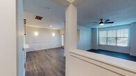 Located at 100 Village Circle Way in Durham, NC, this two-floor residence offers a well-designed layout with contemporary finishes and functional living spaces. The main level features an open-concept living and dining area adorned with durable hardwood-style flooring, wainscoting detail along the walls, and a ceiling fan for added comfort. A structural column adds architectural character to the space, which is brightened by multiple windows fitted with slatted blinds. The kitchen is a standout feature, boasting a peninsula with a white quartz countertop, an undermount sink, and stylish pendant lighting. Gray shaker-style cabinetry pairs with stainless steel appliances, including a refrigerator, range, and microwave. The bathrooms are finished with gray vanity cabinetry, black hardware accents, framed mirrors, and hardwood-style flooring, with one bathroom offering a tiled shower-tub combination. Bedrooms are carpeted and generously sized, with large windows that invite natural light. Multiple walk-in closets with wire shelving systems provide ample storage. A dedicated laundry area with a full-size washer and dryer adds everyday convenience. The overall ambiance is clean, neutral, and move-in ready.