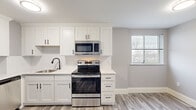 Situated at 101 Cedar St in Providence, Rhode Island, this single-floor space showcases a thoughtfully updated interior with a clean, modern aesthetic. The kitchen is a standout feature, outfitted with white shaker-style cabinetry accented by matte black hardware, white quartz countertops, and a full suite of stainless steel appliances including a refrigerator with ice maker, electric range, over-the-range microwave, and dishwasher. A sleek black-finish sink and wood-look luxury vinyl plank flooring complete the kitchen's contemporary look, which flows openly into the adjacent living area.

The bathroom continues the modern theme with a white vanity, quartz countertop, large mirror, and matte black fixtures and accessories, all set atop matching wood-look flooring. Multiple private rooms feature patterned blue-grey carpet, neutral grey walls, and baseboard heating. Several of these rooms are equipped with wall-mounted air conditioning units and benefit from natural light through windows offering views of the Providence cityscape. Track lighting is present in select areas, adding functional illumination throughout. The overall design is cohesive, clean, and move-in ready.