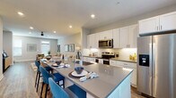 This well-appointed three-floor residence combines contemporary design with functional living across a thoughtfully organized layout. The entry level welcomes guests through a clean, bright foyer with wood-look flooring and carpeted stairs accented by a sleek metal handrail leading to the upper floors. The main living area is anchored by an expansive open-concept kitchen and living room, where white shaker cabinetry, quartz countertops, subway tile backsplash, and stainless steel appliances define a refined culinary space. A generously sized island with bar seating flows seamlessly into the living room, which features hardwood-style flooring and a ceiling fan overhead. A cozy dining nook bathed in natural light from large windows provides an intimate setting for meals. A full bathroom with a white vanity and dark countertop serves the main floor. A dedicated office space stands out with a bold navy accent wall, natural light, and hardwood-style flooring. The upper floors house the bedrooms, including a bright primary suite with oversized windows, a ceiling fan, and direct access to an en-suite area. Additional bedrooms offer comfortable proportions and soft, neutral tones. Throughout the residence, recessed lighting, soft gray walls, and consistent flooring create a cohesive, modern aesthetic.