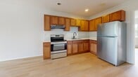 Located at 110 Cedar Road in Amityville, New York, this 520-square-foot, single-floor unit offers a clean and functional layout. The open kitchen/living area features warm wood cabinetry, stainless steel appliances including a refrigerator and range, crown molding, and light hardwood flooring throughout. The 160-square-foot bedroom is bright and airy, with large windows framing lush outdoor tree views, baseboard heating, and a wall-mounted AC unit. White walls and minimalist finishes create a crisp, neutral ambiance across all spaces. A staircase connects the unit to the building's common areas.