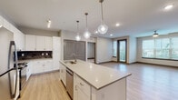 This thoughtfully designed single-floor unit offers a clean, contemporary aesthetic throughout. The open-concept kitchen is a standout feature, anchored by a generous center island with a built-in sink, stainless steel dishwasher, and light quartz countertops. White shaker-style cabinetry with brushed nickel hardware lines the walls, complemented by a dark subway tile backsplash and stainless steel appliances, including a refrigerator and oven. Elegant glass globe pendant lights hang above the island, adding a modern touch. Light wood-look flooring flows seamlessly through the kitchen and into the open living area, which features recessed and track lighting, a ceiling fan, and wide windows that invite abundant natural light and views of surrounding greenery.

The bedrooms are finished with plush carpeting, ceiling fans, and large windows framing outdoor views, creating a calm and comfortable atmosphere. Two bathrooms serve the unit: a primary bath appointed with large-format marble-look tile flooring, a glass-enclosed walk-in shower, a single-sink vanity, and direct access to a walk-in closet with built-in shelving; and a secondary bath with a combination tub and shower, a mirrored vanity, and accessible grab bar fixtures. The overall design balances functionality with modern style throughout.