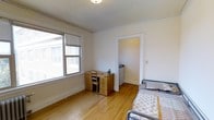 This studio unit offers a practical and efficient single-floor layout designed to maximize every square foot. The main living area features warm hardwood flooring that runs throughout, contributing a clean and cohesive aesthetic to the space. A large window along one wall allows natural light to fill the room, creating a bright and open atmosphere. Crown molding along the ceiling adds a subtle architectural detail that elevates the overall finish of the space.

The layout accommodates a sleeping area and a workspace within the same open room, providing flexibility for how the space is arranged and used. A doorway leads to a separate kitchenette area, which includes a sink and compact refrigerator, offering essential amenities in a neatly contained footprint.

The single bathroom completes the unit, providing all necessary conveniences within a well-organized floor plan. The neutral white walls throughout keep the interior feeling airy and adaptable to a variety of furnishing styles. Overall, this studio presents a straightforward and functional living environment, well-suited for individuals seeking a compact, low-maintenance space with essential features thoughtfully integrated into its design.