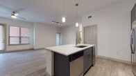 This 2-bedroom, 2-bathroom residence is designed with a contemporary open-concept layout that seamlessly connects the kitchen, dining, and living areas. The kitchen serves as the centerpiece of the home, featuring a large island with a white quartz countertop, an undermount sink, and pendant lighting. Dark charcoal shaker-style cabinetry extends to the ceiling, complemented by a white tile backsplash and a full suite of stainless steel appliances, including a gas range, microwave, dishwasher, and French door refrigerator. A built-in wine/beverage cooler adds an upscale touch. Wood-style plank flooring flows throughout the main living areas, adding warmth and continuity. The spacious living area is accented by track lighting and a ceiling fan. The bedrooms are generously sized, each with ceiling fans and natural light from large windows. The primary bathroom features full-surround tile in a tub/shower combo with a built-in niche, paired with dark cabinetry for storage. The secondary bathroom offers a pedestal sink, mirror, and tile flooring. A dedicated laundry area is also included. The single-floor layout offers an efficient, comfortable flow throughout.