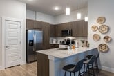 Located at 14914 Vintage Preserve Pkwy in Houston, Texas, this single-floor residence offers a well-designed layout with modern finishes and a cohesive contemporary aesthetic throughout. The open-concept kitchen is a standout feature, boasting rich dark-toned cabinetry, granite countertops, stainless steel appliances, a central island with an undermount sink, pendant lighting, and wood-look flooring that extends into the adjoining living areas. The living room is bright and inviting, benefiting from tall ceilings, a ceiling fan, and large windows with a glass-panel door that allows natural light to flow freely into the space. Multiple bedrooms are present, each carpeted and well-lit with large windows dressed in sheer curtains and blinds. The primary bedroom includes a ceiling fan and ample space for furnishings, while secondary bedrooms offer comfortable layouts with natural light. The bathroom is finished with a granite-top vanity featuring dark wood cabinetry, a framed mirror, and a walk-in glass-enclosed shower with wood-look tile flooring. Neutral wall tones and consistent design elements tie the entire space together, creating a clean, modern, and functional living environment.