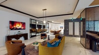 This single-floor amenity space is thoughtfully designed to accommodate a variety of functions within a cohesive, contemporary interior. Large-format marble-look porcelain tile flows throughout, anchoring the open layout and lending a polished, upscale character to the entire floor.

The central lounge area serves as the social heart of the space, furnished with a curved mustard-yellow velvet sofa, cognac leather accent chairs, and layered rugs that define the seating zone. A wall-mounted display screen positioned above a sculptural dark wood console creates a striking focal point. Black-framed glass partition walls divide areas while preserving sightlines and an open feel.

A formal conference and dining area features a long wood table surrounded by upholstered amber chairs, complemented by pendant lighting and framed artwork. Adjacent to this, a series of semi-private banquette booths—lined with textured brick accent walls and warm sconce lighting—offer intimate seating for smaller groups or focused work.

The elevator lobby is distinguished by hexagonal mosaic tile flooring, warm gold wall tiles, brushed steel elevator doors, and curated artwork. A dual water station and thoughtfully placed greenery throughout complete the space, which strikes a balance between professional functionality and lounge-like comfort.