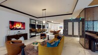 This single-floor amenity space is thoughtfully designed to accommodate a variety of functions within a cohesive, contemporary interior. Large-format marble-look porcelain tile flows throughout, anchoring the open layout and lending a polished, upscale character to the entire floor.

The central lounge area serves as the social heart of the space, furnished with a curved mustard-yellow velvet sofa, cognac leather accent chairs, and layered rugs that define the seating zone. A wall-mounted display screen positioned above a sculptural dark wood console creates a striking focal point. Black-framed glass partition walls divide areas while preserving sightlines and an open feel.

A formal conference and dining area features a long wood table surrounded by upholstered amber chairs, complemented by pendant lighting and framed artwork. Adjacent to this, a series of semi-private banquette booths—lined with textured brick accent walls and warm sconce lighting—offer intimate seating for smaller groups or focused work.

The elevator lobby is distinguished by hexagonal mosaic tile flooring, warm gold wall tiles, brushed steel elevator doors, and curated artwork. A dual water station and thoughtfully placed greenery throughout complete the space, which strikes a balance between professional functionality and lounge-like comfort.