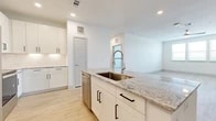 This well-appointed single-story home offers three bedrooms and two bathrooms across a thoughtfully designed open floor plan. The kitchen serves as the centerpiece of the living area, showcasing a large granite-topped island with an undermount sink and a high-arc pull-down faucet, white shaker-style cabinetry with matte black hardware, a subway tile backsplash, a stainless steel dishwasher, and a stainless steel refrigerator. Light wood-look flooring flows through the kitchen and living areas, creating a seamless and airy aesthetic. The spacious living room benefits from natural light and open sightlines to the kitchen.

The primary bedroom is generously sized, featuring plush carpet, a ceiling fan, and access to a walk-in closet with built-in shelving and hanging rods. Its en-suite bathroom is finished with a glass-enclosed walk-in shower with white tile surround, a granite-topped double vanity, and light wood flooring. Additional bedrooms are carpeted, include ceiling fans, and receive natural light through window treatments. A dedicated walk-in closet serves one of the secondary bedrooms. Throughout the home, clean white walls, recessed lighting, and consistent modern finishes contribute to a bright, cohesive, and move-in-ready atmosphere.