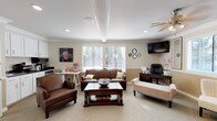 Located in Kent, Washington, this single-story leasing center is designed to provide a comfortable and professional environment for prospective residents. The main lounge area serves as the focal point of the space, featuring warm beige walls accented by a two-tone wainscoting detail and crown molding. Plush carpeting runs throughout, and multiple windows dressed with horizontal blinds allow abundant natural light to fill the room. A ceiling fan overhead adds to the relaxed atmosphere.

The lounge is furnished with rich brown leather sofas, an upholstered bench, and accent chairs arranged around a dark wood coffee table, creating an inviting setting for consultations. A wall-mounted flat-screen television is positioned in the corner for convenience. Adjacent to the seating area, a dedicated desk and office chair provide a functional workspace for leasing staff.

A compact kitchenette is also part of the space, outfitted with white cabinetry, dark granite-style countertops, a stainless steel sink, microwave, and a single-serve coffee maker stocked for guests. A popcorn machine and snack station add a welcoming, hospitality-focused touch.

Additional rooms accessible via white-paneled interior doors offer flexible utility space. Overall, the leasing center presents a polished yet approachable atmosphere suited for welcoming and assisting future residents.