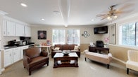 Located in Kent, Washington, this single-story leasing center is designed to provide a comfortable and professional environment for prospective residents. The main lounge area serves as the focal point of the space, featuring warm beige walls accented by a two-tone wainscoting detail and crown molding. Plush carpeting runs throughout, and multiple windows dressed with horizontal blinds allow abundant natural light to fill the room. A ceiling fan overhead adds to the relaxed atmosphere.

The lounge is furnished with rich brown leather sofas, an upholstered bench, and accent chairs arranged around a dark wood coffee table, creating an inviting setting for consultations. A wall-mounted flat-screen television is positioned in the corner for convenience. Adjacent to the seating area, a dedicated desk and office chair provide a functional workspace for leasing staff.

A compact kitchenette is also part of the space, outfitted with white cabinetry, dark granite-style countertops, a stainless steel sink, microwave, and a single-serve coffee maker stocked for guests. A popcorn machine and snack station add a welcoming, hospitality-focused touch.

Additional rooms accessible via white-paneled interior doors offer flexible utility space. Overall, the leasing center presents a polished yet approachable atmosphere suited for welcoming and assisting future residents.