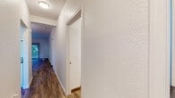 This single-floor residence offers a well-organized layout connecting living, dining, kitchen, and bedroom areas through a hallway finished with wood-style flooring and textured walls. The living area is bright and open, featuring sliding glass doors fitted with vertical blinds that invite natural light and provide access to an outdoor view. The space flows naturally into the dining area, which is highlighted by a modern chandelier and a pass-through counter connecting directly to the kitchen.

The kitchen is well-appointed with white shaker-style cabinetry extending to the ceiling, granite-look countertops, and a full suite of stainless steel appliances including a refrigerator, range, over-the-range microwave, and dishwasher. A stainless steel sink with a window pass-through adds both function and a sense of openness.

The bedroom is generously sized, carpeted in neutral tones, and includes a window overlooking greenery, along with access to a closet. The bathroom features a granite-top vanity with white cabinetry, a vessel sink, and wood-style flooring, with a louvered closet door visible nearby. Throughout, the consistent use of neutral tones, textured walls, and coordinated finishes creates a cohesive and functional living environment.