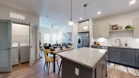This single-floor residence offers a thoughtfully designed open-concept layout that seamlessly connects the kitchen, dining, and living areas. The kitchen is a standout feature, showcasing two-tone cabinetry with charcoal lower cabinets and soft gray upper cabinets, granite countertops, a classic white subway tile backsplash, and a full suite of stainless steel appliances. A large central island with pendant lighting serves as both a functional workspace and a focal point for the space. Wood-look flooring runs throughout the main living areas, adding warmth and continuity. The dining area sits adjacent to the kitchen, while the living room offers abundant natural light through multiple windows and a glass door that opens to a private exterior space. Taller-than-standard ceilings in the living area enhance the sense of openness. The bedroom is a comfortable retreat, featuring plush carpeting, a ceiling fan, and large windows fitted with blinds for light control. The primary bathroom is generously sized, with a dedicated vanity area featuring granite countertops and hardwood flooring, leading to a separate commode and bathing area. Clean white walls and recessed lighting throughout the residence contribute to a bright, contemporary ambiance that is both functional and inviting.