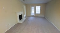 This single-floor residence offers a comfortable and functional layout designed for easy everyday living. The main living area is a standout feature of the home, centered around a classic white-mantled fireplace with a brick surround and hearth, adding a warm and traditional character to the space. Soft, neutral-toned wall-to-wall carpeting extends throughout the room, providing a cozy underfoot feel and complementing the light beige walls that create a clean, understated backdrop. Natural light flows generously into the living area through a glass-panel exterior door and an adjacent large window, brightening the interior and offering a connection to the outdoors. The open feel of the living space allows for flexible furniture arrangements to suit a variety of needs. A doorway leads to additional areas of the home, suggesting a practical and well-organized floor plan. The overall ambiance of the space is calm and inviting, with neutral finishes throughout that provide a versatile canvas for personalization. This residence presents a straightforward, functional design with classic residential details that offer lasting appeal.