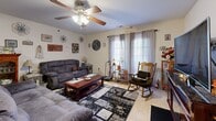 Located at 1300 Hazel Ln in Farmington, MO, this single-floor home offers a practical and comfortable layout across two bedrooms, two bathrooms, a kitchen, living room, and a dedicated office space. The living room is a welcoming area featuring light tile flooring, a ceiling fan with light fixture, and windows dressed with sheer curtains that allow natural light to fill the room. An electric fireplace built into a rich wood entertainment console serves as a focal point on the opposite wall. The kitchen is well-equipped with warm cherry wood cabinetry, dark granite-style countertops, a dining table with seating, and tile flooring — providing ample storage and prep space. The primary bedroom includes a ceiling fan, carpet flooring, and enough space to accommodate a full bedroom suite. The second bedroom offers carpeted floors and a curtained window. The office is a versatile room with carpet, a ceiling fan, a window for natural light, and space for a desk and exercise equipment. The bathroom features a wood vanity with a large mirror, a tub-shower combination, and tile flooring.
