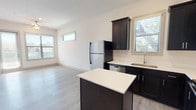 This single-floor, one-bedroom, one-bathroom unit offers a thoughtfully designed layout that maximizes functionality within a compact footprint. The kitchen serves as a focal point of the space, featuring dark espresso cabinetry with ample upper and lower storage, crisp white countertops, and a full suite of stainless steel appliances including a refrigerator, electric range, microwave, and dishwasher. A central island provides additional prep space and casual dining potential. Light wood-look flooring flows seamlessly throughout the main living areas, lending warmth and visual continuity.

The living area is bright and open, benefiting from multiple windows fitted with blinds that allow for natural light control. The bedroom is well-proportioned, featuring a ceiling fan, a large window with outdoor views, and access to a generous walk-in closet outfitted with built-in shelving units and dual hanging rods for organized storage.

The bathroom is finished with clean white subway tile surrounding a full soaking tub and shower combination, complemented by neutral tile flooring. The overall aesthetic throughout is modern and clean, with a neutral color palette that creates a calm, move-in-ready atmosphere.