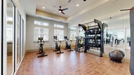 Located at 400 Hidden Palm Cir in Kissimmee, Florida, this fitness center offers a spacious and well-appointed workout facility designed to accommodate a variety of exercise routines. The single-level space is bright and inviting, featuring elevated ceilings with tray detailing and ceiling fans that promote airflow throughout. Large windows lined with blinds line the walls, flooding the interior with abundant natural light and creating an open, energizing atmosphere.

The fitness center is organized into distinct workout zones. A dedicated cycling area houses multiple stationary spin bikes, each equipped with digital screens for interactive training sessions. Adjacent to this area is a comprehensive Training Zone featuring a fully stocked dumbbell rack with a wide range of weights, kettlebells, medicine balls, and TRX suspension training equipment. A separate section contains strength training machines, including cable systems and weight benches, catering to a full range of resistance exercises.

Full-length mirrors span entire wall sections, enhancing the sense of space while allowing users to monitor their form. The durable tile flooring throughout is both functional and easy to maintain. A portable workout pad provides additional flexibility for functional training. The thoughtful layout and diverse equipment selection make this facility suitable for users of all fitness levels.