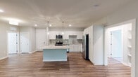 This well-appointed single-floor residence offers a thoughtfully designed layout with modern finishes throughout. The heart of the home is an open-concept kitchen, outfitted with crisp white shaker cabinetry, light stone countertops, and a decorative gray subway tile backsplash. A full suite of stainless steel appliances — including a range, microwave, dishwasher, and french door refrigerator — provides both functionality and style. Pendant lighting illuminates a central island, making it an ideal space for dining or entertaining. Warm wood-look flooring extends throughout the main living areas, adding a cohesive and inviting feel. The bedrooms are carpeted for comfort, each featuring neutral toned walls, blinds-fitted windows with views of surrounding greenery, and ceiling fans for year-round climate control. A spacious walk-in closet with wire shelving and hanging rods offers generous storage. The bathrooms are finished with white cabinetry, stone-topped vanities, and tile flooring. One bathroom includes a tub-shower combination with white tile surround, while another features a wide double-sink vanity. The overall design aesthetic is clean, contemporary, and move-in ready.