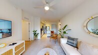 This single-floor residence showcases a clean, contemporary design characterized by crisp white walls, large-format tile flooring, and an abundance of natural light throughout. The open-concept layout connects the living, dining, and kitchen areas into one cohesive, airy space anchored by a ceiling fan overhead.

The kitchen is outfitted with floor-to-ceiling flat-front white cabinetry, grey quartz countertops, a subtle glass tile backsplash, and a full suite of stainless steel appliances including a refrigerator, electric range, built-in microwave, and dishwasher. A peninsula with seating extends from the kitchen, serving as both a dining and casual gathering space.

The living area is bright and welcoming, with a large sliding glass door opening onto a private balcony that overlooks lush greenery and the surrounding outdoor environment, bringing the outdoors in.

The bedrooms are calm and restful, each featuring ceiling fans, wide windows with garden views, and light wood-toned flooring. The bathroom is finished with white cabinetry, a dark countertop, a full tub and shower combination, and recessed lighting, maintaining the unit's consistent modern aesthetic throughout.