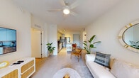 This single-floor residence showcases a clean, contemporary design characterized by crisp white walls, large-format tile flooring, and an abundance of natural light throughout. The open-concept layout connects the living, dining, and kitchen areas into one cohesive, airy space anchored by a ceiling fan overhead.

The kitchen is outfitted with floor-to-ceiling flat-front white cabinetry, grey quartz countertops, a subtle glass tile backsplash, and a full suite of stainless steel appliances including a refrigerator, electric range, built-in microwave, and dishwasher. A peninsula with seating extends from the kitchen, serving as both a dining and casual gathering space.

The living area is bright and welcoming, with a large sliding glass door opening onto a private balcony that overlooks lush greenery and the surrounding outdoor environment, bringing the outdoors in.

The bedrooms are calm and restful, each featuring ceiling fans, wide windows with garden views, and light wood-toned flooring. The bathroom is finished with white cabinetry, a dark countertop, a full tub and shower combination, and recessed lighting, maintaining the unit's consistent modern aesthetic throughout.