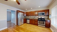 Located at 114 Franklin St in Morristown, NJ, this two-bedroom, one-bathroom residence offers a well-organized single-floor layout with warm hardwood flooring running throughout. The combined dining room and kitchen serves as a functional centerpiece, featuring rich wood cabinetry, granite countertops, a stone tile backsplash, and a full suite of stainless steel appliances including a gas range, built-in microwave, dishwasher, and refrigerator. Recessed lighting and crown molding add a polished finish to this space. The living room is bright and open, with natural light streaming through multiple windows. Both bedrooms are comfortably sized, each equipped with ceiling fans, wall-mounted air conditioning units, and radiator heating. The primary bedroom includes a double sliding-door closet, while four closets total are distributed throughout the unit, providing ample storage. The bathroom is finished with full tile walls, a tile floor, a soaking tub with shower, and a wood-vanity with an oval mirror. An in-unit laundry area adds everyday convenience. Neutral gray walls and gleaming hardwood floors lend the entire residence a clean, cohesive aesthetic.