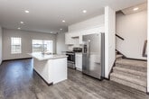 This well-designed two-story home offers a thoughtful layout that balances everyday functionality with modern finishes throughout. The main floor centers around an open-concept kitchen and living area, where rich hardwood-style flooring flows seamlessly underfoot. The kitchen is outfitted with white shaker-style cabinetry, light granite countertops, and a full suite of stainless steel appliances including a gas range and a side-by-side refrigerator. A central island with a built-in sink adds both workspace and a natural gathering point. Recessed lighting illuminates the area, while a sliding glass door and adjacent window in the living area flood the space with natural light and provide access to outdoor views. A convenient half bathroom is also located on the main floor. A carpeted staircase leads to the upper level, where the bedrooms are situated. Each bedroom features plush carpet flooring, ceiling fans, and windows that invite natural light. The upper floor is served by two full bathrooms — one with a walk-in shower and soaking tub, and another with a shower/tub combo. Dark accent doors and trim provide a clean contrast against the neutral wall tones throughout, giving the home a cohesive and contemporary feel.