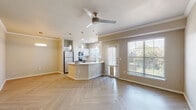 This single-floor residence offers a thoughtfully designed open-concept layout that seamlessly connects the kitchen, dining, and living areas. The kitchen is a standout feature, equipped with stainless steel appliances including a refrigerator, range, microwave, and dishwasher, all complemented by crisp white cabinetry and light quartz countertops. A peninsula island provides additional prep space and casual seating, while stylish pendant lights hang overhead to create a warm, focused ambiance. The living area is generously proportioned, with crown molding accents, a ceiling fan, and large windows fitted with blinds that invite ample natural light and offer views of greenery outside. A glass-paneled door leads to an outdoor area, further enhancing the connection to the exterior. Throughout the main living spaces, distinctive herringbone-patterned light wood flooring adds a refined, modern touch. The bedroom is carpeted for comfort and features a ceiling fan and a large window. The bathroom is well-appointed with an extended dual-sink vanity topped with white quartz, a backlit mirror, ample cabinetry, a tiled shower, and matching herringbone flooring. The overall palette of warm neutral tones and clean white finishes lends the space a bright, contemporary, and welcoming atmosphere.