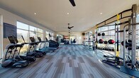 The Sugarloaf Grove Fitness Center in Lawrenceville, Georgia is a thoughtfully designed, single-floor facility that provides residents with a comprehensive and energizing workout environment. Floor-to-ceiling windows and large glass garage-style doors line the perimeter, flooding the space with natural light and offering expansive views of the outdoor pool area and landscaped grounds, creating a bright and motivating atmosphere.

The fitness center is equipped with a wide array of True-brand cardio machines, including multiple treadmills, ellipticals, a stair climber, and additional cardio equipment, all positioned to take full advantage of the outdoor views. A dedicated strength training zone features power racks with free weights and barbells, cable machines, and adjustable benches for a complete resistance training experience.

A functional training area rounds out the facility, outfitted with TRX suspension trainers, battle ropes, kettlebells of varying weights, medicine balls, and a multi-use rig — ideal for high-intensity and circuit-style workouts. Large mirrors are positioned throughout the space to enhance the sense of openness. Overhead ceiling fans and recessed lighting maintain comfort throughout the room. The durable, striped carpet tile flooring ties the space together, providing both practicality and a modern aesthetic.