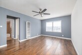 Located on Crenshaw Boulevard in Los Angeles, this well-appointed 1-bedroom, 1-bathroom unit offers a thoughtfully designed single-floor layout. Warm hardwood flooring runs throughout the main living and bedroom areas, lending a cohesive and inviting feel to the space. The living area is bright and airy, featuring soft blue-gray walls, white trim, and a ceiling fan with integrated lighting. A wall-mounted heating unit and a window with horizontal blinds complete this comfortable room.

The galley-style kitchen is efficiently designed with dark espresso cabinetry, light granite countertops, a mosaic tile backsplash, and tile flooring. Stainless steel appliances—including a gas range, microwave, and full-size refrigerator—provide modern functionality, while a double-basin sink adds everyday convenience.

The bedroom offers a comfortable footprint with the same warm hardwood flooring, a ceiling fan, natural light from a window, and a built-in mirrored closet with overhead cabinetry for ample storage. A separate closet and hallway provide additional organizational space throughout the unit.

The bathroom features a tub and shower combination surrounded by large-format stone-look tile, paired with a white vanity and clean, neutral finishes. The overall design is practical, clean, and well-maintained throughout.