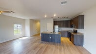 This two-story home offers a well-organized layout with distinct living spaces spread across both levels. The main floor centers around an open-concept kitchen and living area bathed in natural light from sliding glass doors and adjacent windows, which frame outdoor views. Light wood-look flooring flows throughout the main level, complementing the neutral wall tones and creating a bright, cohesive atmosphere. The kitchen is outfitted with dark wood cabinetry, granite countertops, stainless steel appliances, and a central island with a built-in sink, providing ample workspace and storage. Track lighting and recessed fixtures illuminate the area effectively. A ceiling fan anchors the spacious living area. The upper level is accessed via a carpeted staircase featuring a white-painted balustrade and newel posts. Bedrooms upstairs are carpeted and filled with natural light from double-hung windows, with at least one room offering views of a nearby body of water. Closets with double doors provide practical storage. Two bathrooms serve the home—one featuring a tub-shower combination with large-format tile surround, and the other a walk-in tile shower, both finished with clean white tile flooring and dark wood vanities.