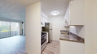 This single-floor residence offers a clean, functional layout with thoughtful finishes throughout. The kitchen is designed for efficiency, featuring white shaker-style cabinetry, granite-look countertops, stainless steel appliances including a refrigerator and range, a stainless steel sink, and light wood-look flooring — all beneath a textured ceiling with flush-mount lighting. The galley-style configuration maximizes storage and counter space.

The living area is bright and open, anchored by wide sliding glass doors with vertical blinds that invite natural light and provide access to an outdoor space. A wall-mounted air conditioning unit ensures year-round comfort, and the light wood-look flooring continues throughout, lending a cohesive feel to the space.

The bedroom is a generously sized, quiet retreat finished with neutral carpet and crisp white walls, offering a comfortable and versatile space. A hallway connects the rooms with ease, maintaining a smooth flow throughout the unit.

The bathroom is well-equipped with a white tiled tub-shower combination, a white vanity with granite-look countertop, and stainless steel grab bars for added accessibility and safety. The wood-look flooring ties the space together with the rest of the residence, creating a consistent and polished aesthetic throughout.