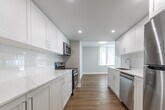 This well-appointed 2-bedroom, 1-bathroom unit at 220 Dennistoun Street in Welland, Ontario, offers a clean, modern aesthetic throughout its thoughtfully designed single-floor layout. Warm wood-look flooring flows seamlessly across every room, complemented by a crisp white and light grey palette that creates a bright, welcoming atmosphere.

The expansive combined living and dining area is a standout feature, bathed in natural light through floor-to-ceiling wraparound windows fitted with vertical blinds. These large windows frame lush green outdoor views and allow sunlight to stream across the space throughout the day. Baseboard heating runs along the exterior walls, ensuring year-round comfort.

The galley-style kitchen is well-equipped and thoughtfully finished, featuring white shaker cabinetry, light countertops, a stainless steel sink, and stainless steel appliances including a refrigerator, dishwasher, and range. Recessed lighting adds a polished touch overhead.

The primary bedroom is generously sized, offering a large sliding-door closet and access to the connecting hallway. The second bedroom features its own window with outdoor views and baseboard heating. A central hallway connects all rooms efficiently.

The bathroom is finished in a clean, minimalist style with a white vanity, toilet, and a full bathtub-shower combination, all set on matching wood-look flooring.