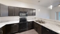 Located at 1908 Fox Rd in Rapid City, South Dakota, this single-floor 2-bedroom, 2-bathroom residence offers a clean, modern design with a practical and efficient layout. The open-concept living, dining, and kitchen area serves as the heart of the home, featuring dark espresso cabinetry, marble-look countertops, black appliances including a range, microwave, dishwasher, and refrigerator, along with wood-look vinyl flooring and a stylish pendant light fixture. A hallway connects the main living area to the private quarters, with two carpeted bedrooms each offering natural light through window blinds and access to closets. The primary bedroom includes its own dedicated bathroom with a walk-in shower, dark vanity cabinetry, and a single sink. The second bathroom is equipped with a full soaking tub and shower combo, matching the clean white aesthetic found throughout. An in-unit laundry area provides added convenience, and a utility room and entrance complete the thoughtfully organized floor plan. The interior is finished with neutral tones, white trim, and consistent flooring materials, creating a cohesive and move-in-ready living environment.