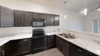 Located at 1908 Fox Rd in Rapid City, South Dakota, this single-floor 2-bedroom, 2-bathroom residence offers a clean, modern design with a practical and efficient layout. The open-concept living, dining, and kitchen area serves as the heart of the home, featuring dark espresso cabinetry, marble-look countertops, black appliances including a range, microwave, dishwasher, and refrigerator, along with wood-look vinyl flooring and a stylish pendant light fixture. A hallway connects the main living area to the private quarters, with two carpeted bedrooms each offering natural light through window blinds and access to closets. The primary bedroom includes its own dedicated bathroom with a walk-in shower, dark vanity cabinetry, and a single sink. The second bathroom is equipped with a full soaking tub and shower combo, matching the clean white aesthetic found throughout. An in-unit laundry area provides added convenience, and a utility room and entrance complete the thoughtfully organized floor plan. The interior is finished with neutral tones, white trim, and consistent flooring materials, creating a cohesive and move-in-ready living environment.