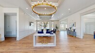 Located at 29803 Hardiman Rd in Madison, Alabama, this single-story community clubhouse delivers a polished, upscale atmosphere through thoughtful architectural detailing and a cohesive blue and gold color palette. The grand main hall serves as the centerpiece of the space, anchored by a striking oversized gold candelabra chandelier suspended beneath a coffered ceiling. White wainscoting panels line the walls, complementing warm-toned hardwood flooring that flows throughout the entire facility. Generous floor-to-ceiling windows and French doors flood the interior with natural light while providing views of an outdoor pool area.

The lounge area features plush navy velvet seating arranged around a sleek white console table, creating an inviting gathering space. A dedicated dining room accommodates a large rectangular table with upholstered chairs, accented by a bold botanical-patterned wallcovering in blue and cream tones. The fully equipped kitchen showcases deep blue cabinetry with gold hardware, quartz countertops, stainless steel appliances, open wood shelving, and a large island. Additional service counter space with matching cabinetry and open shelving provides ample functionality. Together, these spaces create a refined yet welcoming environment suitable for community gatherings and events.