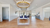 Located at 29803 Hardiman Rd in Madison, Alabama, this single-story community clubhouse delivers a polished, upscale atmosphere through thoughtful architectural detailing and a cohesive blue and gold color palette. The grand main hall serves as the centerpiece of the space, anchored by a striking oversized gold candelabra chandelier suspended beneath a coffered ceiling. White wainscoting panels line the walls, complementing warm-toned hardwood flooring that flows throughout the entire facility. Generous floor-to-ceiling windows and French doors flood the interior with natural light while providing views of an outdoor pool area.

The lounge area features plush navy velvet seating arranged around a sleek white console table, creating an inviting gathering space. A dedicated dining room accommodates a large rectangular table with upholstered chairs, accented by a bold botanical-patterned wallcovering in blue and cream tones. The fully equipped kitchen showcases deep blue cabinetry with gold hardware, quartz countertops, stainless steel appliances, open wood shelving, and a large island. Additional service counter space with matching cabinetry and open shelving provides ample functionality. Together, these spaces create a refined yet welcoming environment suitable for community gatherings and events.