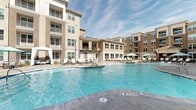 Located at 2599 Evans Rd in Morrisville, NC, this outdoor amenity space is designed to deliver a resort-style living experience within a modern multi-story residential community. The centerpiece is a generously sized swimming pool with crystal-clear blue water, shallow in-pool lounge areas, and entry steps that invite leisurely relaxation. Surrounding the pool is a well-appointed sun deck furnished with rows of sling-back chaise lounges and shaded cabanas, offering ample space for sunbathing and socializing under open skies.

A covered outdoor lounge area provides a comfortable retreat with plush seating and views directly overlooking the pool and surrounding building façades, which feature a contemporary mix of brick, siding, and large windows. Lush landscaped beds with fresh mulch and ornamental shrubs line the pool perimeter, adding greenery and visual warmth to the space.

A separate courtyard features a row of rustic wooden posts strung with overhead café lights, creating an inviting, pedestrian-friendly promenade. A circular fire pit seating area anchors this zone, providing an ideal gathering spot during cooler evenings. Together, these outdoor spaces form a cohesive and thoughtfully designed amenity environment tailored for active community living.