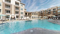 Located at 2599 Evans Rd in Morrisville, NC, this outdoor amenity space is designed to deliver a resort-style living experience within a modern multi-story residential community. The centerpiece is a generously sized swimming pool with crystal-clear blue water, shallow in-pool lounge areas, and entry steps that invite leisurely relaxation. Surrounding the pool is a well-appointed sun deck furnished with rows of sling-back chaise lounges and shaded cabanas, offering ample space for sunbathing and socializing under open skies.

A covered outdoor lounge area provides a comfortable retreat with plush seating and views directly overlooking the pool and surrounding building façades, which feature a contemporary mix of brick, siding, and large windows. Lush landscaped beds with fresh mulch and ornamental shrubs line the pool perimeter, adding greenery and visual warmth to the space.

A separate courtyard features a row of rustic wooden posts strung with overhead café lights, creating an inviting, pedestrian-friendly promenade. A circular fire pit seating area anchors this zone, providing an ideal gathering spot during cooler evenings. Together, these outdoor spaces form a cohesive and thoughtfully designed amenity environment tailored for active community living.