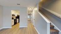 This two-story home offers a thoughtfully designed layout with a clean, contemporary aesthetic throughout. The main level welcomes you with a bright, open living area featuring light luxury vinyl plank flooring and large windows that allow ample natural light to fill the space. The living area flows directly into the kitchen, which is equipped with white shaker-style cabinetry accented by matte black hardware, marble-look countertops, a gas range, and a range hood — a practical setup well-suited for everyday cooking. A hallway on the main level leads to additional rooms and a bathroom featuring a walk-in shower stall, a toilet, and light wood-tone flooring with a clean, minimal finish. A staircase connects to the upper floor, where carpeted bedrooms provide a comfortable, quiet retreat. Each bedroom includes windows with blinds for natural light and privacy, and at least one room features a ceiling fan. A second bathroom on the upper level includes a soaking tub and shower surround. Neutral gray tones are used consistently throughout the home, creating a cohesive and move-in-ready atmosphere across both floors.