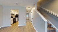 This two-story home offers a thoughtfully designed layout with a clean, contemporary aesthetic throughout. The main level welcomes you with a bright, open living area featuring light luxury vinyl plank flooring and large windows that allow ample natural light to fill the space. The living area flows directly into the kitchen, which is equipped with white shaker-style cabinetry accented by matte black hardware, marble-look countertops, a gas range, and a range hood — a practical setup well-suited for everyday cooking. A hallway on the main level leads to additional rooms and a bathroom featuring a walk-in shower stall, a toilet, and light wood-tone flooring with a clean, minimal finish. A staircase connects to the upper floor, where carpeted bedrooms provide a comfortable, quiet retreat. Each bedroom includes windows with blinds for natural light and privacy, and at least one room features a ceiling fan. A second bathroom on the upper level includes a soaking tub and shower surround. Neutral gray tones are used consistently throughout the home, creating a cohesive and move-in-ready atmosphere across both floors.