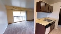 This 2-bedroom, 1-bathroom unit is arranged on a single floor, offering a straightforward and functional layout. The living area is carpeted and spacious, anchored by a large sliding glass door that floods the room with natural light and provides direct access to a private balcony. The balcony overlooks an outdoor setting with mature trees visible in the background, adding a sense of openness to the space.

Adjacent to the living area, the kitchen features dark wood cabinetry both above and below the counter, offering ample storage. A built-in sink is integrated into the light-colored countertop, and the kitchen connects seamlessly to the main living space through an open pass-through style layout, making it easy to move between areas. Overhead ventilation is provided throughout via ceiling vents.

The unit's color palette is neutral, with light blue-gray walls and beige tones throughout, creating a calm and understated atmosphere. The carpeted floors in the living space add warmth, while the overall design reflects a practical, no-frills approach to residential living. Two bedrooms and a full bathroom complete the unit's footprint.