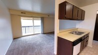 This 2-bedroom, 1-bathroom unit is arranged on a single floor, offering a straightforward and functional layout. The living area is carpeted and spacious, anchored by a large sliding glass door that floods the room with natural light and provides direct access to a private balcony. The balcony overlooks an outdoor setting with mature trees visible in the background, adding a sense of openness to the space.

Adjacent to the living area, the kitchen features dark wood cabinetry both above and below the counter, offering ample storage. A built-in sink is integrated into the light-colored countertop, and the kitchen connects seamlessly to the main living space through an open pass-through style layout, making it easy to move between areas. Overhead ventilation is provided throughout via ceiling vents.

The unit's color palette is neutral, with light blue-gray walls and beige tones throughout, creating a calm and understated atmosphere. The carpeted floors in the living space add warmth, while the overall design reflects a practical, no-frills approach to residential living. Two bedrooms and a full bathroom complete the unit's footprint.
