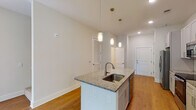 Located at 305 Oberlin Rd in Raleigh, NC, this thoughtfully designed two-story residence combines modern finishes with a functional, open layout. The main level features a well-appointed kitchen at its heart, centered around a granite-topped island with an undermount sink and elegant pendant lighting. White shaker-style cabinetry lines the walls, complemented by a herringbone tile backsplash, stainless steel appliances — including a French door refrigerator, electric range, and over-the-range microwave — and warm hardwood-style flooring that carries throughout the main living areas. The adjacent living and dining spaces are bright and open, with large windows inviting natural light and views of the surrounding neighborhood. A staircase connects the two floors, with the upper level offering carpeted bedroom spaces, each equipped with ceiling fans and ample natural light through generously sized windows. The bathrooms are finished with granite-topped vanities, undermount sinks, framed mirrors, and wood-style flooring, providing a clean and polished aesthetic. Throughout both floors, neutral tones, recessed lighting, and clean architectural lines create a cohesive, contemporary ambiance well-suited for comfortable everyday living.