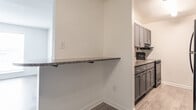 Located at 549 Adams Drinks in Newport News, Virginia, this single-floor residence offers a well-organized layout with consistent wood-style flooring throughout. The open living and dining area is bright and welcoming, featuring a ceiling fan with light fixture, natural light from a large front-facing window, and a seamless connection to the kitchen via a peninsula counter with a dark granite surface — ideal for casual dining or meal prep. The kitchen is outfitted with gray cabinetry, granite countertops, stainless black appliances including an electric range and dishwasher, and an overhead microwave range hood, providing both style and function. A hallway connects the main living area to the private quarters, where two bedrooms offer wood-style flooring, neutral white walls, textured ceilings, and windows overlooking the surrounding neighborhood. Each bedroom includes closet access and is filled with natural light. The bathroom is neatly appointed with subway tile wainscoting, a granite-topped vanity with a gray cabinet base, a mirrored medicine cabinet, and a tub-shower combination with a curved curtain rod. Clean white walls and wood-style flooring complete the cohesive aesthetic found throughout this well-maintained home.