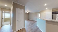 This single-floor residence offers a thoughtfully designed open-concept layout that seamlessly connects the main living areas. The living room features warm hardwood-style flooring, crown molding, a ceiling fan, and a sliding glass door that opens to a private balcony, flooding the space with natural light and providing outdoor views. Adjacent to the living area, the kitchen is well-equipped with dark espresso cabinetry, granite-style countertops, stainless steel appliances including a range, over-the-range microwave, and dishwasher, as well as a peninsula with a breakfast bar that enhances the open flow of the space. The bedrooms are generously sized with plush carpeting and feature ample closet space, including a walk-in closet in the primary bedroom. The bathrooms are finished with dark wood vanities topped with granite-style countertops and large mirrors, with one bathroom offering a walk-in shower. Neutral warm-toned walls throughout create a cohesive and inviting ambiance, while crown molding and clean white trim add a refined architectural detail. The overall design balances functional living with modern finishes, making this a comfortable and attractive space.