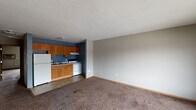 This single-floor unit in Marion, Iowa offers a straightforward, functional layout well-suited for everyday living. The open-concept living and kitchen area provides a seamless flow between spaces, with the living room featuring neutral gray walls, wall-to-wall carpeting, and a baseboard heating system. A paneled entry door with wood trim offers direct access to the main living space.

The kitchen is efficiently designed with warm oak cabinetry above and below the counter, a double-basin sink, a white electric range with overhead ventilation, and a full-size refrigerator. Bold blue accent walls give the kitchen a distinct look, complemented by tile-style flooring that separates it from the carpeted living area.

The bedrooms are carpeted and finished with the same neutral gray palette, each equipped with baseboard heaters for individual climate control. Large sliding windows in the bedrooms allow natural light to fill the rooms and offer views of the surrounding exterior. Wood-toned interior doors and light wood baseboards provide consistent, cohesive detailing throughout. The textured ceilings and simple, clean finishes contribute to the overall practical and no-frills character of this Marion, Iowa residence.