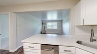 This single-floor, one-bedroom, one-bathroom residence offers a practical and functional layout with thoughtfully designed spaces throughout. The kitchen is a standout feature, equipped with crisp white shaker-style cabinetry, a white subway tile backsplash, and a full suite of stainless steel appliances including a refrigerator, electric range, and over-the-range microwave. Wood-look plank flooring runs through the kitchen and living areas, lending a warm, cohesive feel to the space. The living room is bright and open, featuring neutral walls, baseboard heating, and a clean, versatile canvas for various furniture arrangements. Natural light filters in through windows that offer views of surrounding greenery, adding a welcoming, airy quality to the interior. The bedroom is generously sized and finished with plush carpeting and a window that brings in natural light, creating a comfortable and restful retreat. A baseboard heating unit ensures year-round comfort. The bathroom includes a full tub-shower combination, toilet, and wood-look flooring, finished in a clean, neutral palette. Throughout the residence, neutral tones and clean lines create a consistent, move-in-ready aesthetic that is both practical and inviting.