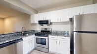 Located at River Ridge Drive in Augusta, Georgia, this one-bedroom, one-bathroom residence offers a practical and modern layout across a single floor. The open kitchen and living room area serves as the heart of the home, where the kitchen stands out with crisp white shaker cabinetry extending to the ceiling for ample storage, granite countertops with subtle veining, and a full suite of stainless steel appliances including a gas range, over-the-range microwave, and refrigerator. Light wood-style flooring runs throughout the space, lending a clean and cohesive aesthetic. The living room benefits from a large window that invites natural light and frames views of the surrounding greenery, creating a bright and welcoming atmosphere. The bedroom offers a comfortable footprint with wood-style tile flooring and a generously sized sliding-door closet equipped with a hanging rod and shelving. The bathroom mirrors the kitchen's design language, featuring a granite-topped white vanity with an undermount sink, a framed mirror, and a full tub-shower combination. Neutral wall tones and consistent finishes throughout the residence create a unified, move-in-ready environment.