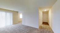 Located at 2G Raylon Dr., this single-floor residence offers a clean, functional layout designed for comfortable everyday living. The interior is finished with neutral-toned carpeting throughout the main living areas, lending a cohesive and understated aesthetic. A central dividing wall creates a natural separation between the open living space and an adjacent room, allowing for distinct functional zones while maintaining an overall sense of openness. Natural light filters in through a window visible in the connected room, brightening the space with a soft, airy feel. The entryway area transitions to hard flooring, providing a practical and easy-to-maintain surface near the main door. Smooth, light-colored walls and standard ceiling heights contribute to a simple, move-in-ready environment. A hallway leads to additional rooms and closet spaces, offering convenient access throughout the unit. The overall ambiance is clean and neutral, making it an adaptable space well-suited to a variety of furnishing styles and personal tastes.