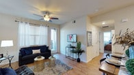 This single-floor residence features two bedrooms and two bathrooms within a thoughtfully designed layout. The living area serves as the heart of the space, showcasing light wood-tone flooring that extends throughout, contributing to a warm and cohesive aesthetic. Neutral-toned walls enhance the sense of openness, while a ceiling fan with an integrated light fixture provides both comfort and functionality overhead.

Natural light flows into the living room through large windows dressed with white curtains, and a glass-paneled door opens to a private outdoor balcony, offering a seamless connection to the exterior. The living area comfortably accommodates a sofa and accent tables, creating an inviting atmosphere for relaxation.

A hallway visible from the living space leads to additional rooms, including the bedrooms and bathrooms, maintaining a clear and accessible floor plan. The overall design balances practicality with contemporary style, featuring clean lines, neutral finishes, and modern fixtures throughout. The combination of natural light, wood-look flooring, and an open layout gives the space a bright, airy ambiance suitable for everyday living.