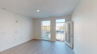 Located at 734 Wayne St in Cincinnati's 45206 neighborhood, this single-floor residence showcases a clean, contemporary design with an open-concept living and kitchen area bathed in natural light. Light-toned luxury vinyl plank flooring runs throughout the main living spaces, complementing the bright white walls and modern aesthetic.

The kitchen is a standout feature, centered around a large island with a stainless steel undermount sink and pendant lighting overhead. White shaker-style cabinetry extends to the ceiling, paired with stainless steel appliances including a range, over-the-range microwave, and refrigerator. The open layout connects the kitchen seamlessly to the living area, which opens directly onto a private balcony through a glass-paned door, offering views of the surrounding neighborhood.

The bedroom is carpeted for comfort and includes a closet with built-in shelving. A window provides natural light and neighborhood views. The unit includes two bathrooms — one featuring a full tub and shower combination with a white vanity, and another with a dedicated vanity area with ample cabinet storage. An in-unit stacked washer and dryer is also present. The thoughtful layout and modern finishes make this a well-appointed, move-in-ready space.